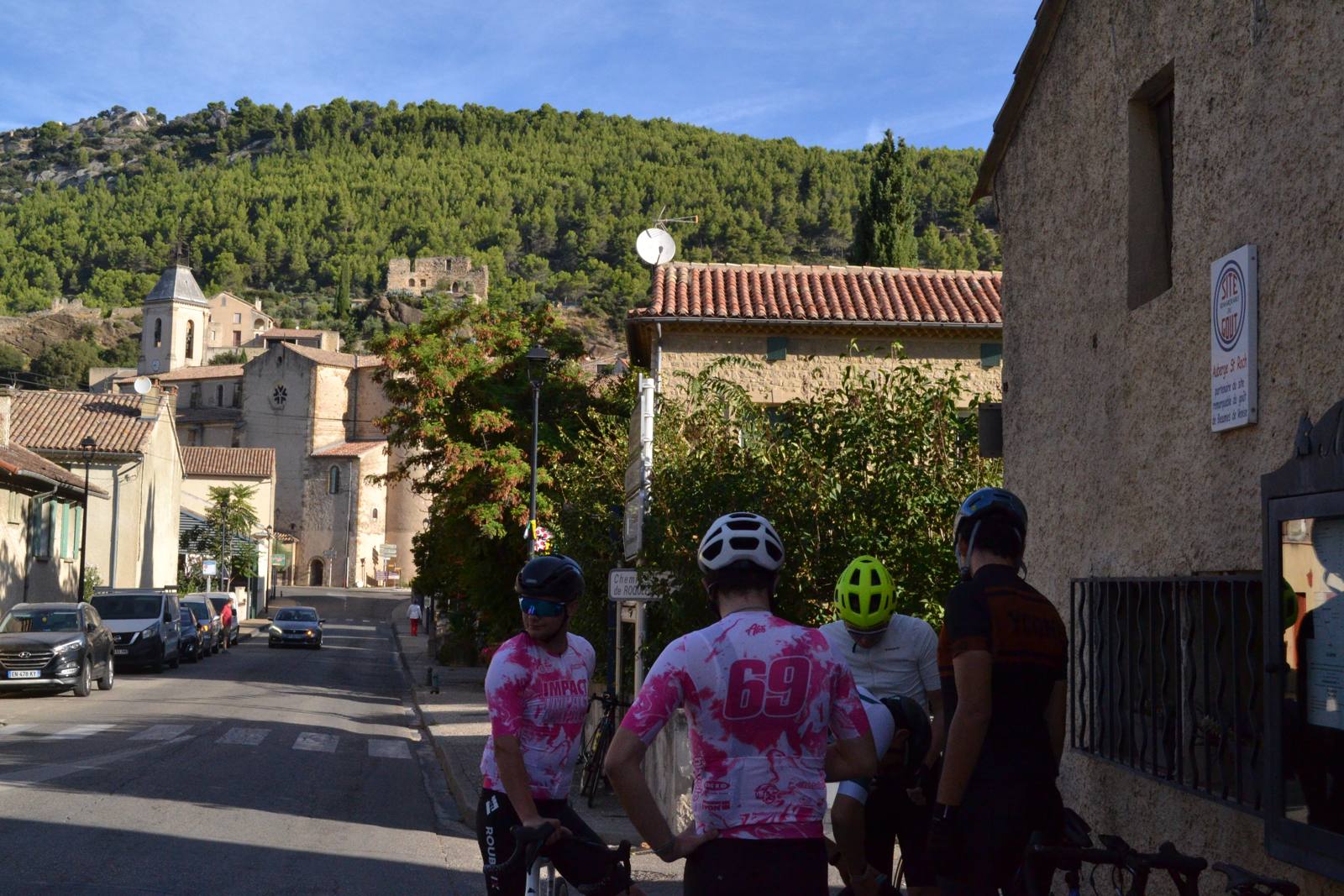 Groupe de cyclistes à l'arrêt dans une rue de village au pied d'une colline boisée